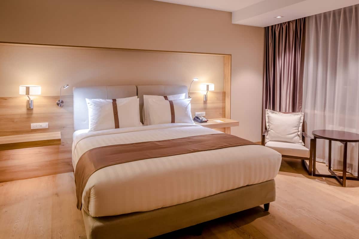 A hotel room with a large bed, two bedside tables with lamps, a chair, and a small table.