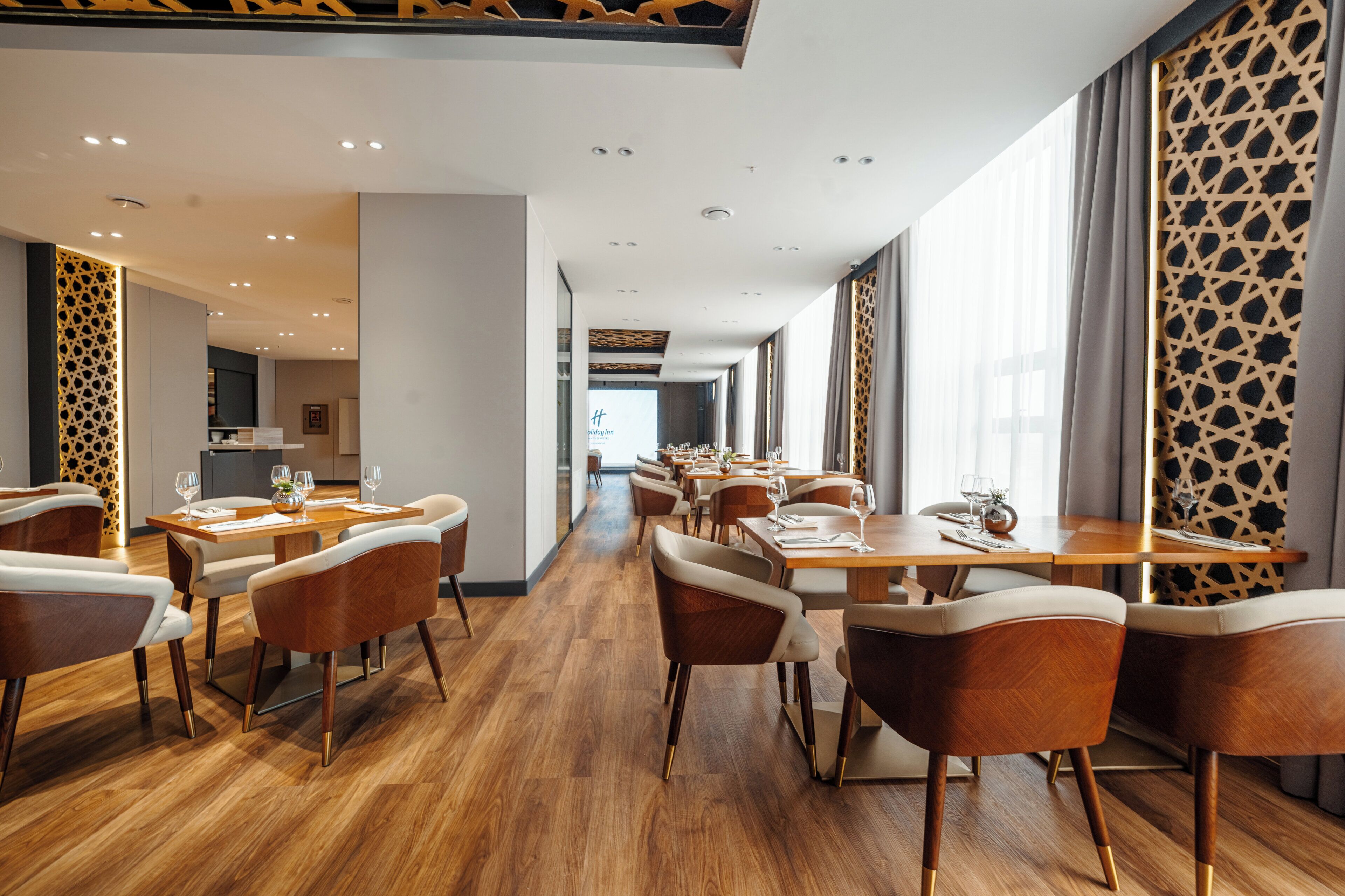 A hotel dining area with wooden flooring, modern furniture, and large windows.