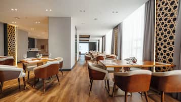 A hotel dining area with wooden flooring, modern furniture, and large windows.