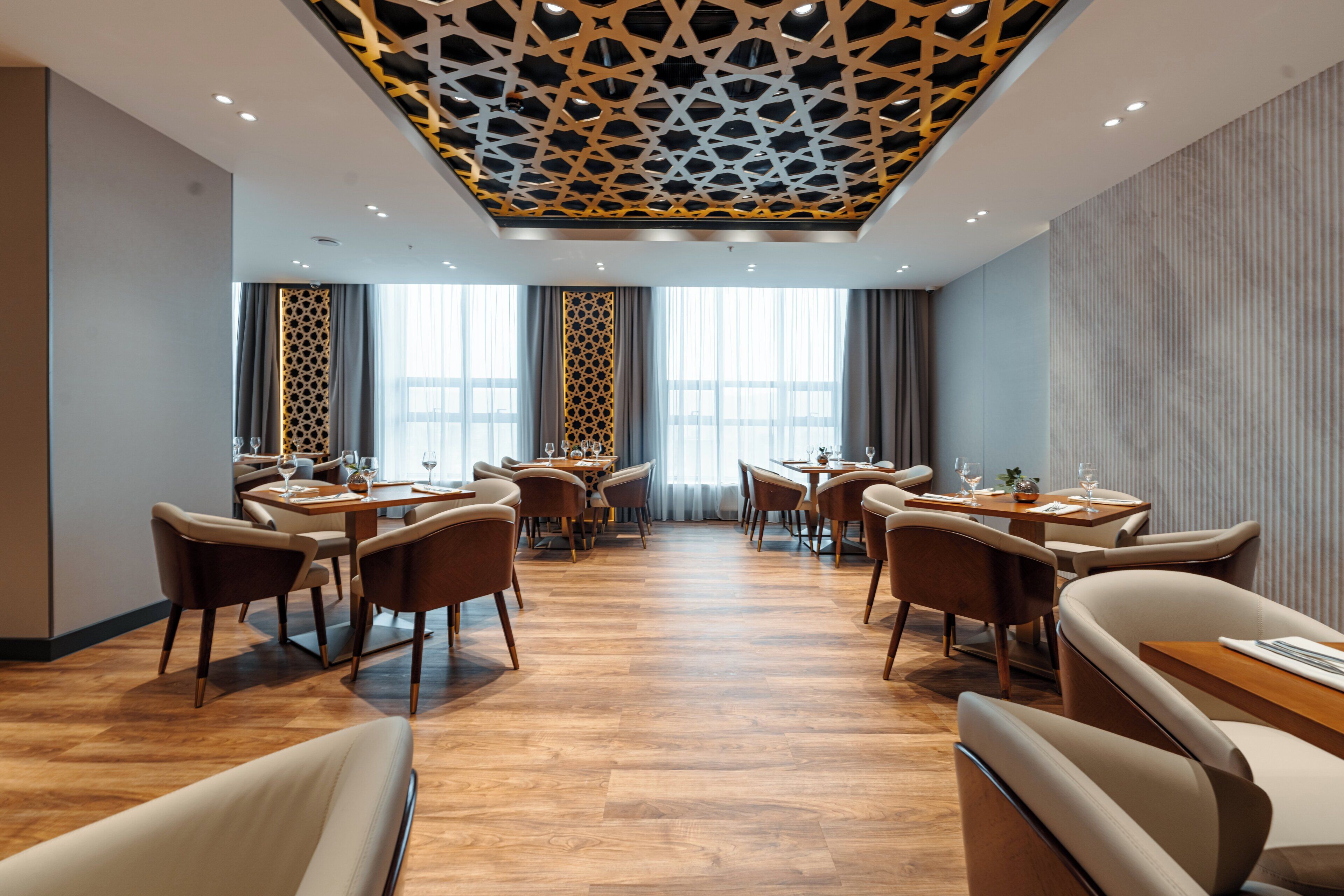 A modern dining area with multiple tables and chairs, a patterned ceiling, and large windows.