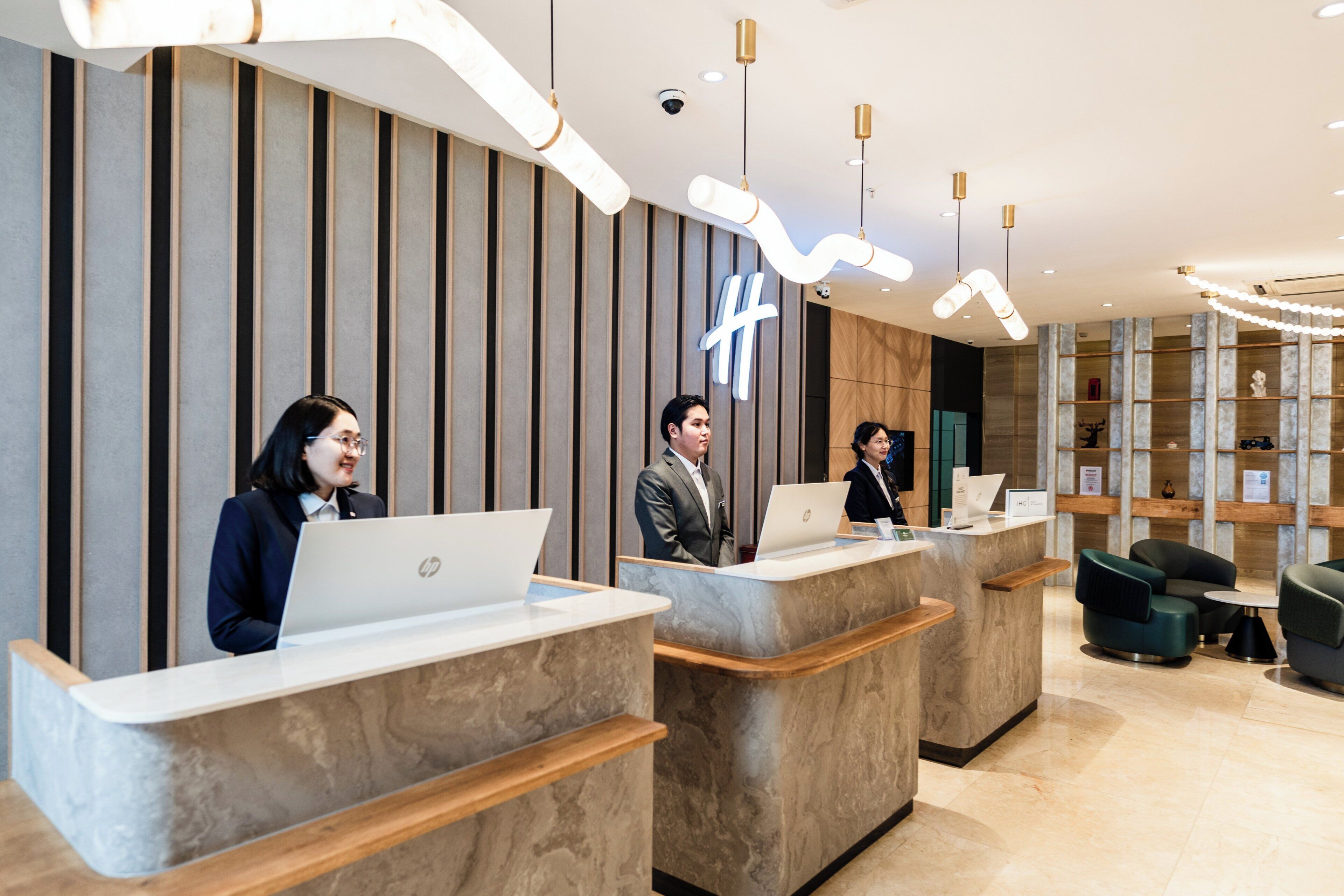 A reception desk area with three HP laptops, a modern interior design with vertical wooden panels, and a reception desk with a nameplate.