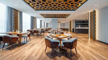 A modern restaurant with wooden flooring, multiple dining tables, and a patterned ceiling.