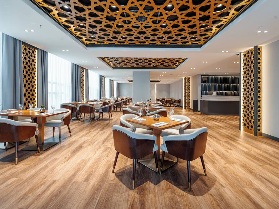 A modern restaurant with wooden flooring, multiple dining tables, and a patterned ceiling.