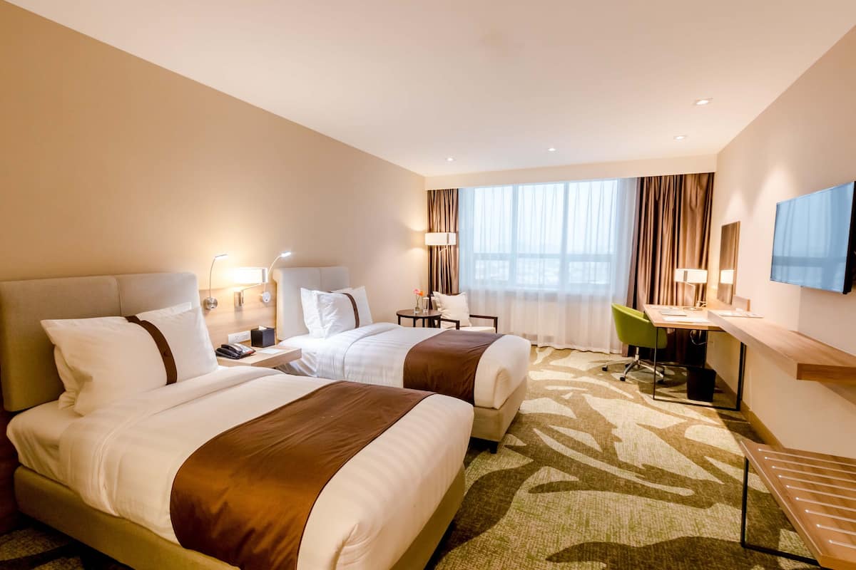 A hotel room with two beds, a desk, a chair, a TV, and a window with curtains.