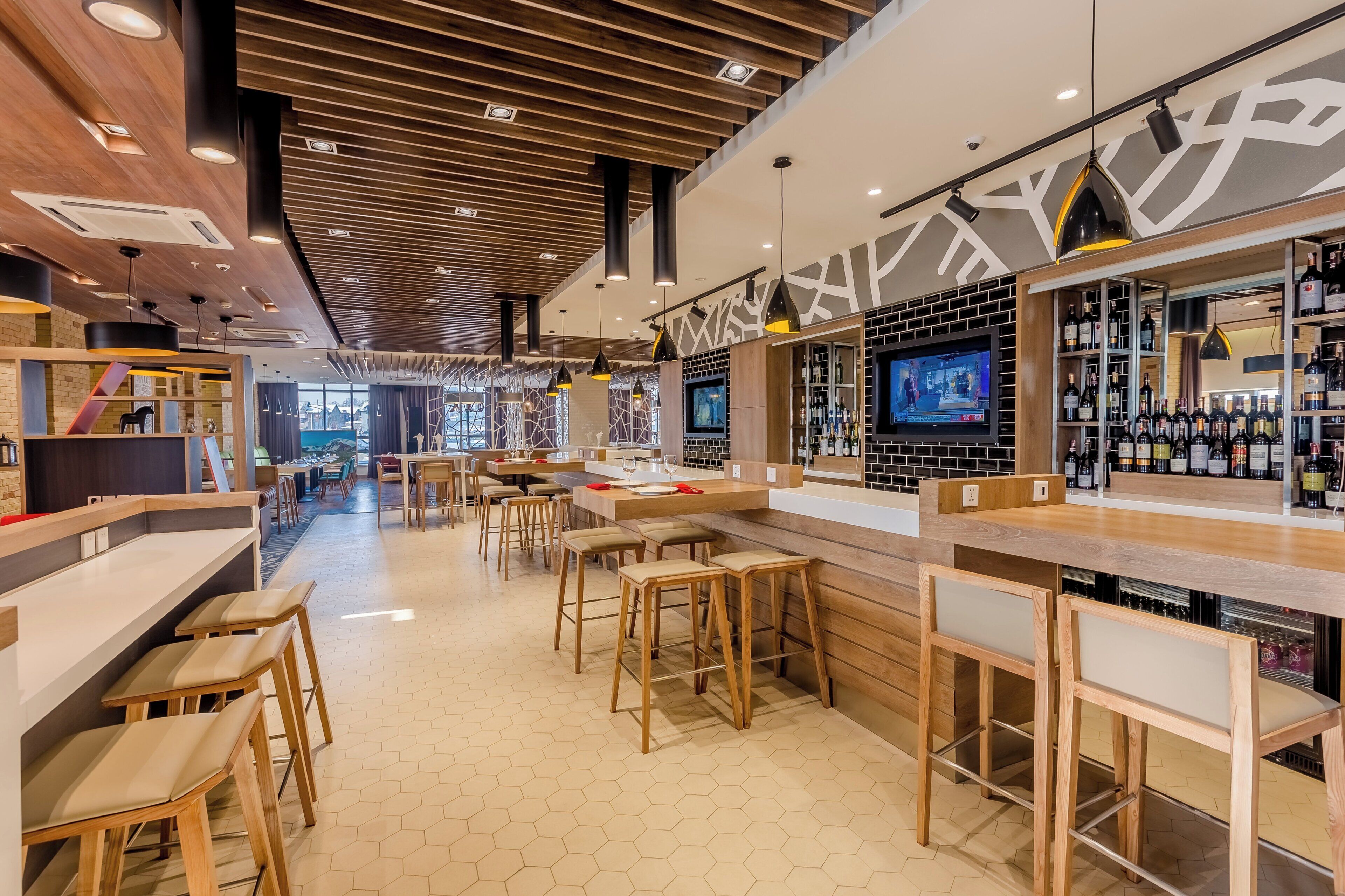 A modern bar area with hexagonal floor tiles, wooden furniture, and a television screen.
