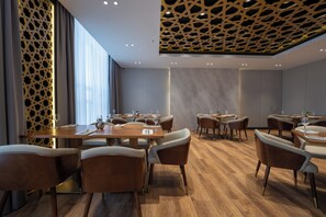 A modern dining area with wooden tables and chairs, a patterned ceiling, and large windows.