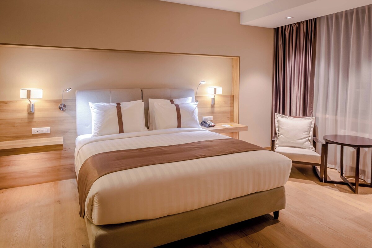 Ein Hotelzimmer mit einem großen Bett, Nachttischen, einem Sessel und einem kleinen Tisch.