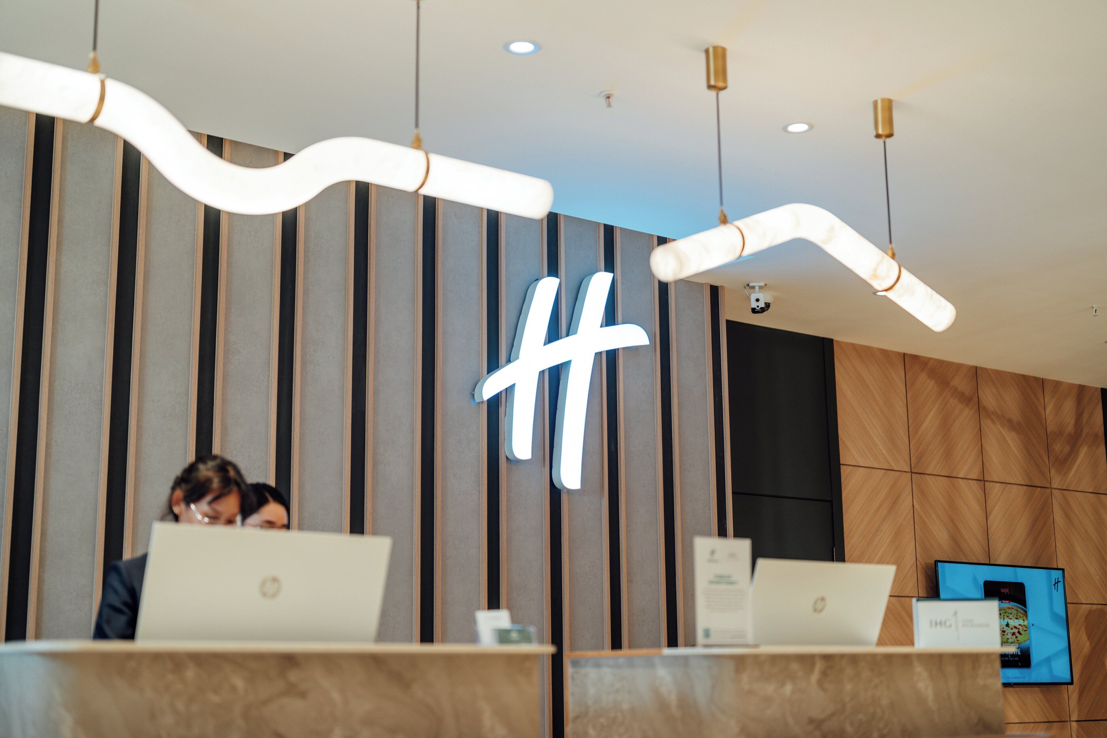 Un mostrador de recepción con dos computadoras portátiles, un llamativo letrero iluminado con el símbolo numeral y un diseño interior moderno con paneles de madera verticales.