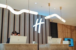 A reception desk with two laptops, a large illuminated hashtag sign, and a modern interior design with vertical wooden panels.