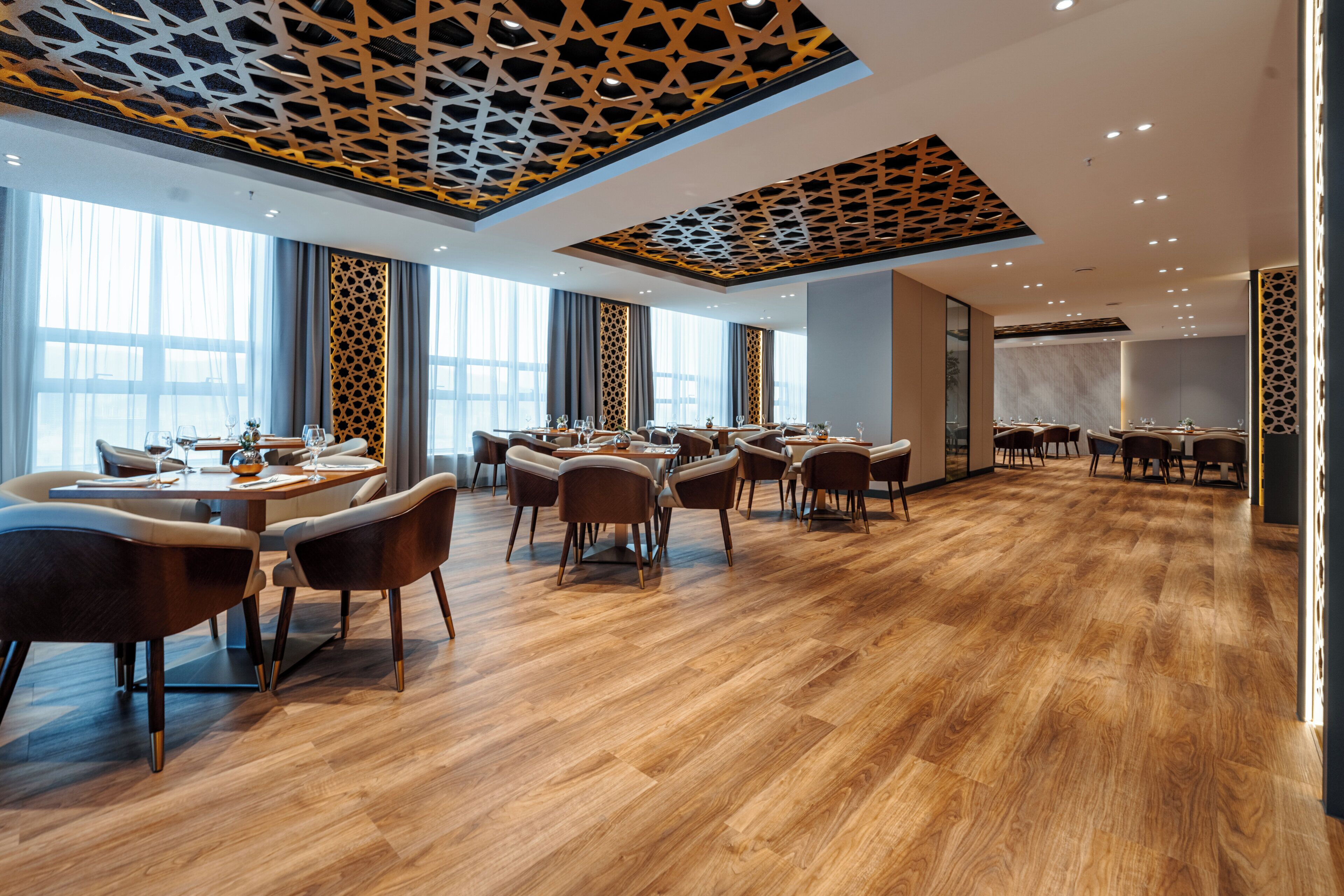 A modern dining area with wooden flooring, multiple tables, and chairs.