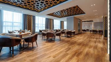 A modern dining area with wooden flooring, multiple tables, and chairs.