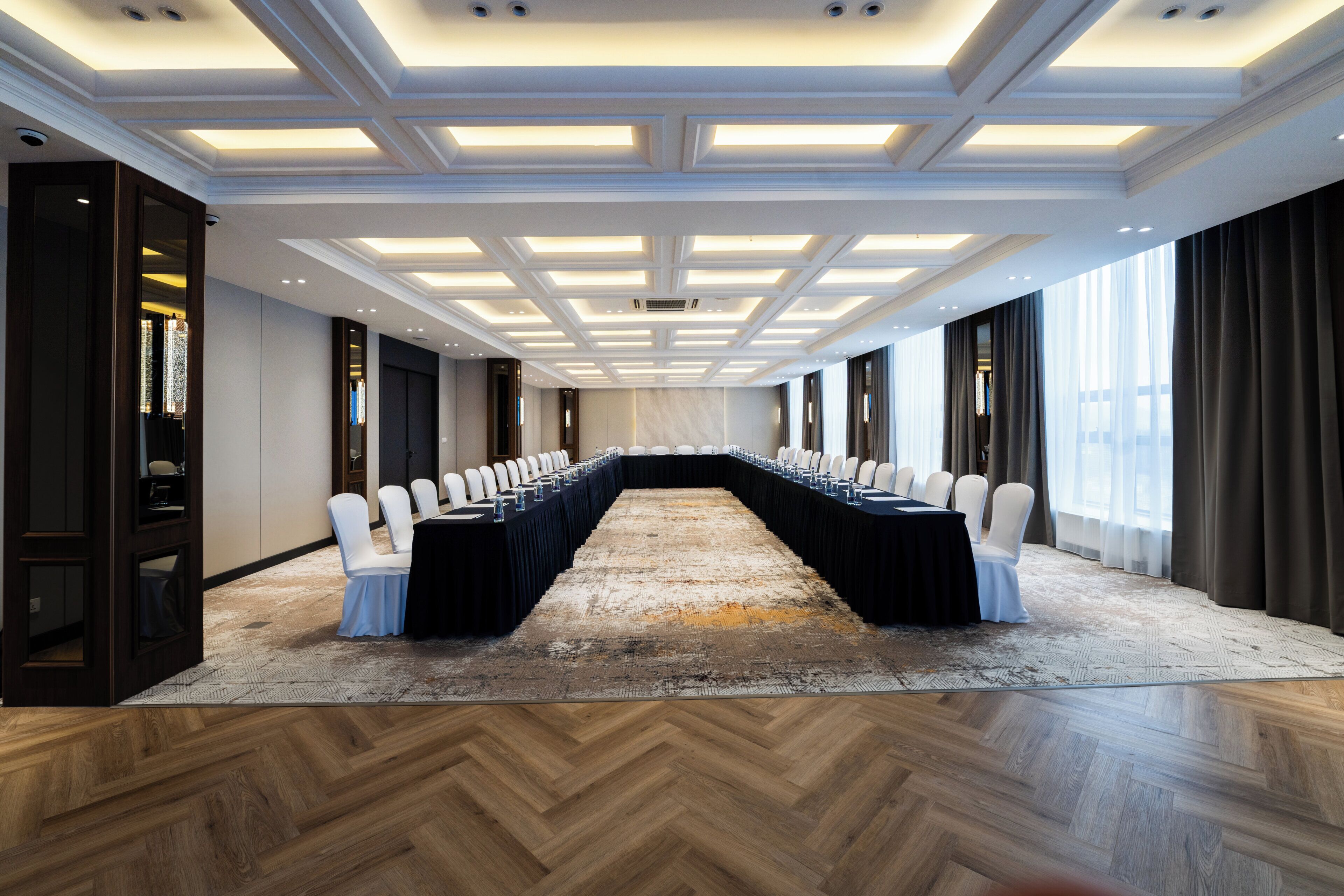 Una sala de conferencias con una larga mesa, sillas blancas y una alfombra estampada.