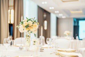 Una mesa de banquete dispuesta con manteles blancos, cristalería transparente y un centro de mesa con flores y velas.