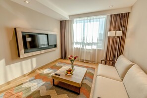 Ein modernes Wohnzimmer mit einem an der Wand befestigten Flachbildfernseher, einer Couch, einem Couchtisch mit Blumen und einem gemusterten Teppich.
