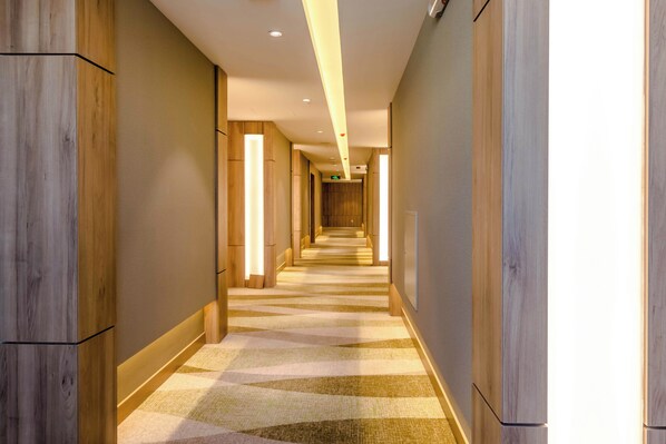 Passadís d'hotel modern amb panells de fusta, una catifes amb dibuixos i il·luminació encastrada.