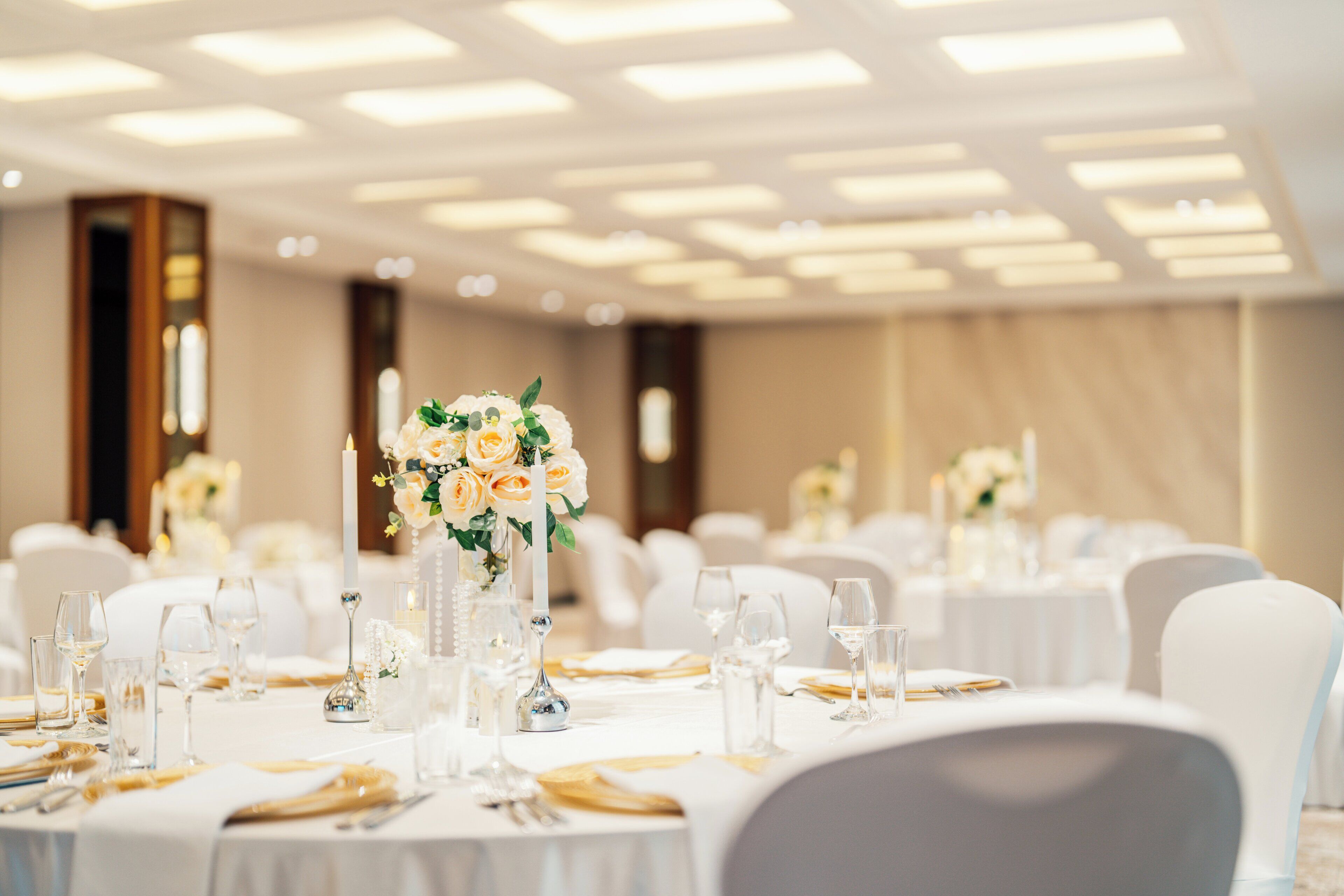 Uma sala de banquetes com mesas redondas dispostas para refeições, com toalhas brancas e copos.