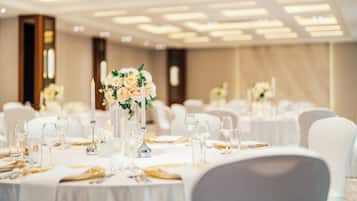 Uma sala de banquetes com mesas redondas dispostas para refeições, com toalhas brancas e copos.
