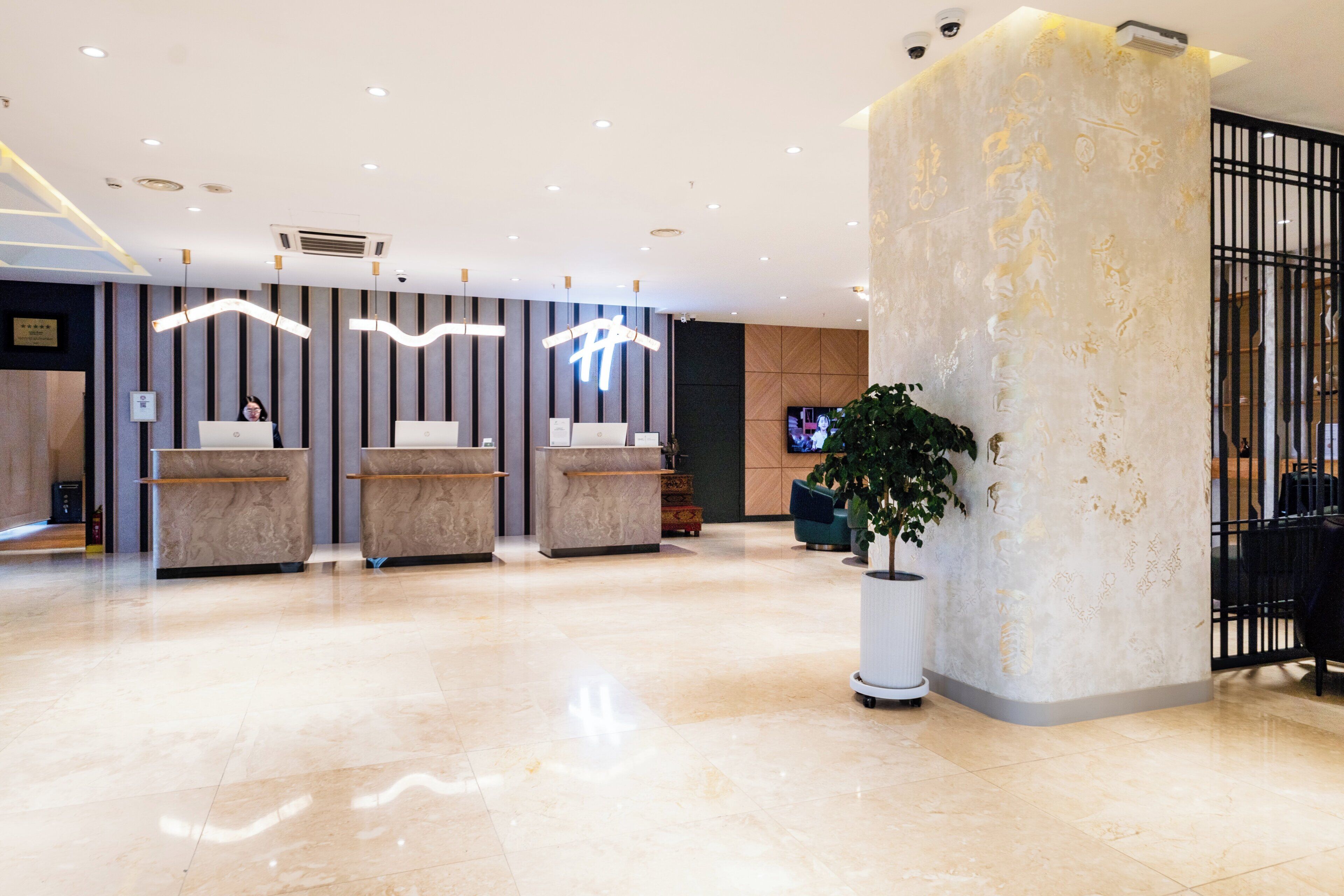A reception area with a modern design, featuring a reception desk, a large potted plant, and a wall-mounted television.