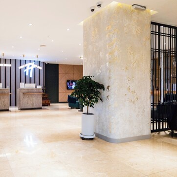 A reception area with a modern design, featuring a reception desk, a large potted plant, and a wall-mounted television.