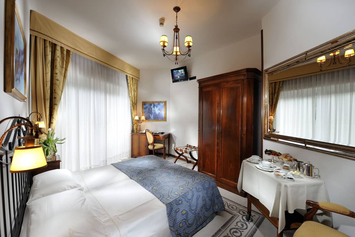 Une chambre d’hôtel comprenant un lit, un bureau, une armoire, une table à manger avec des articles pour le petit-déjeuner et un téléviseur fixé au mur.