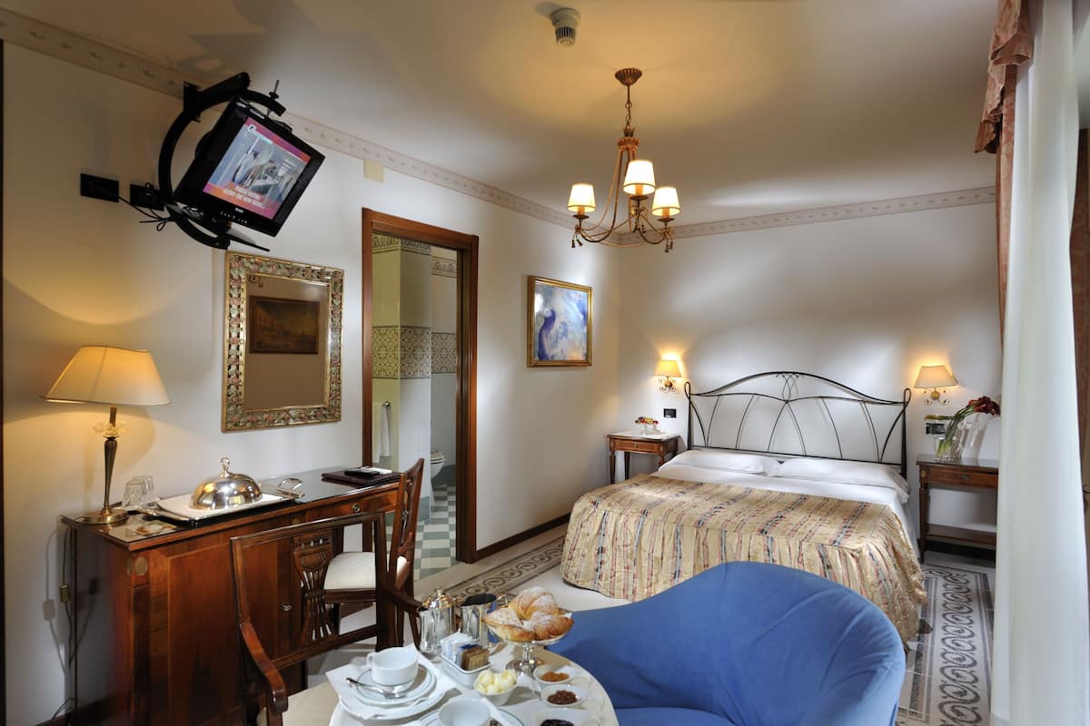 Une chambre d’hôtel avec un lit, un bureau doté d’une lampe, un téléviseur fixé au mur et un lustre.