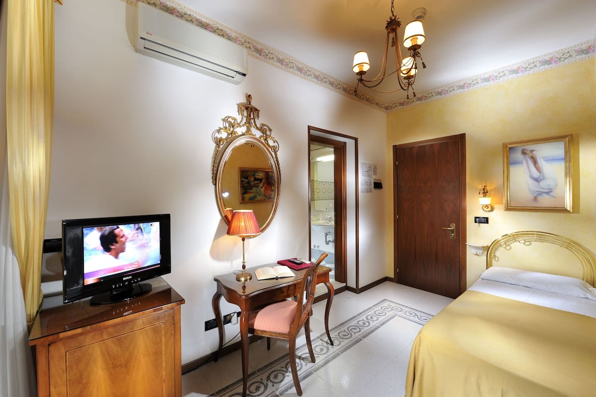Une chambre d’hôtel équipée d’une télévision, d’un bureau, d’une chaise, d’un lit et d’un miroir.