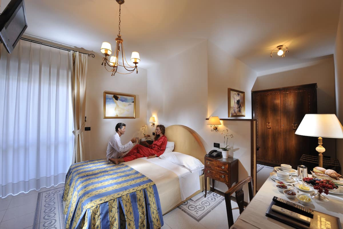 Une chambre d’hôtel comprenant un lit, une table de chevet, une lampe et un coin repas avec une table mise pour le petit-déjeuner.