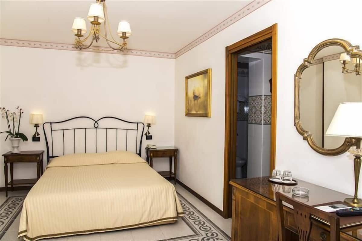 Une chambre d’hôtel avec un lit, des tables de chevet, un miroir, un lustre et un tableau au mur.