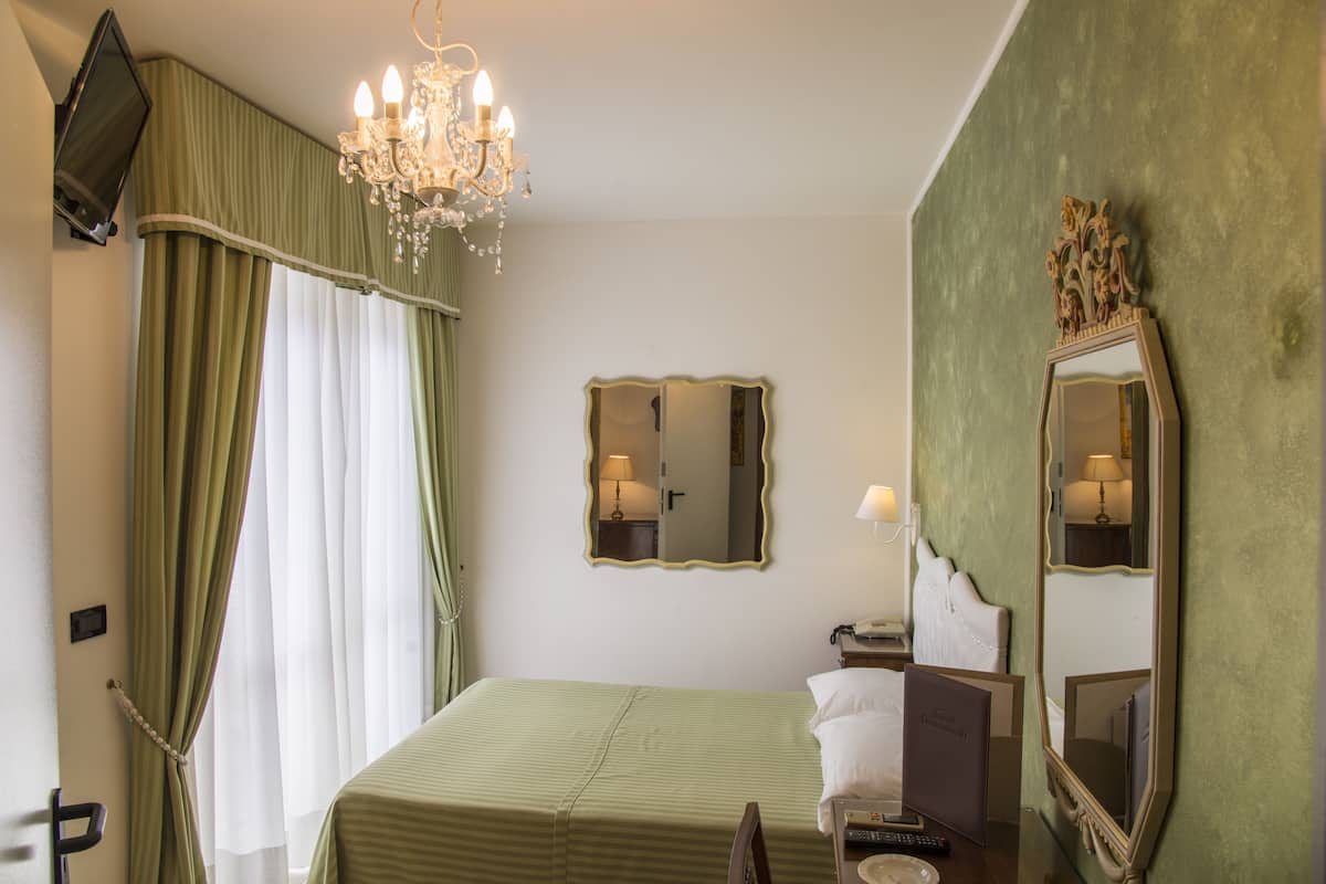 Une chambre d’hôtel avec un lit, un lustre, un miroir et un téléviseur fixé au mur.