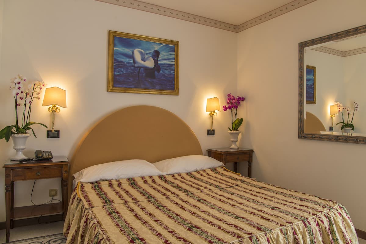 Une chambre d’hôtel avec un grand lit, deux tables de chevet avec des lampes, un tableau au-dessus du lit et un miroir au mur.