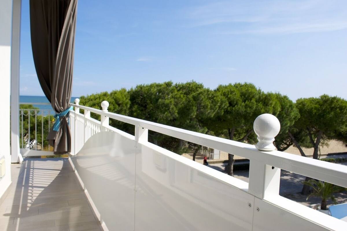 Un balcon doté d’une balustrade blanche, offrant une vue sur une plage et des arbres.