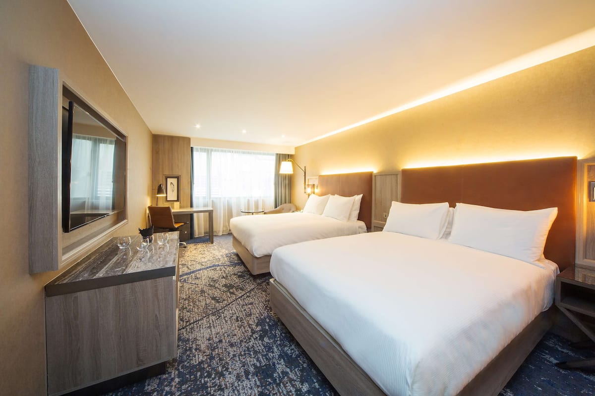 Habitación de hotel con dos camas, un escritorio, un televisor y un ventanal grande.