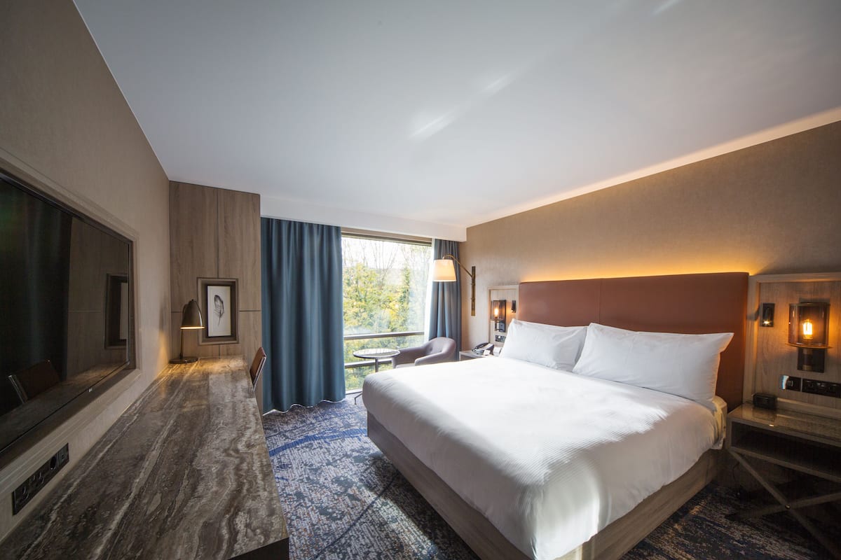 Habitación de hotel con una cama grande, un escritorio, una silla, un televisor y una ventana con cortinas.