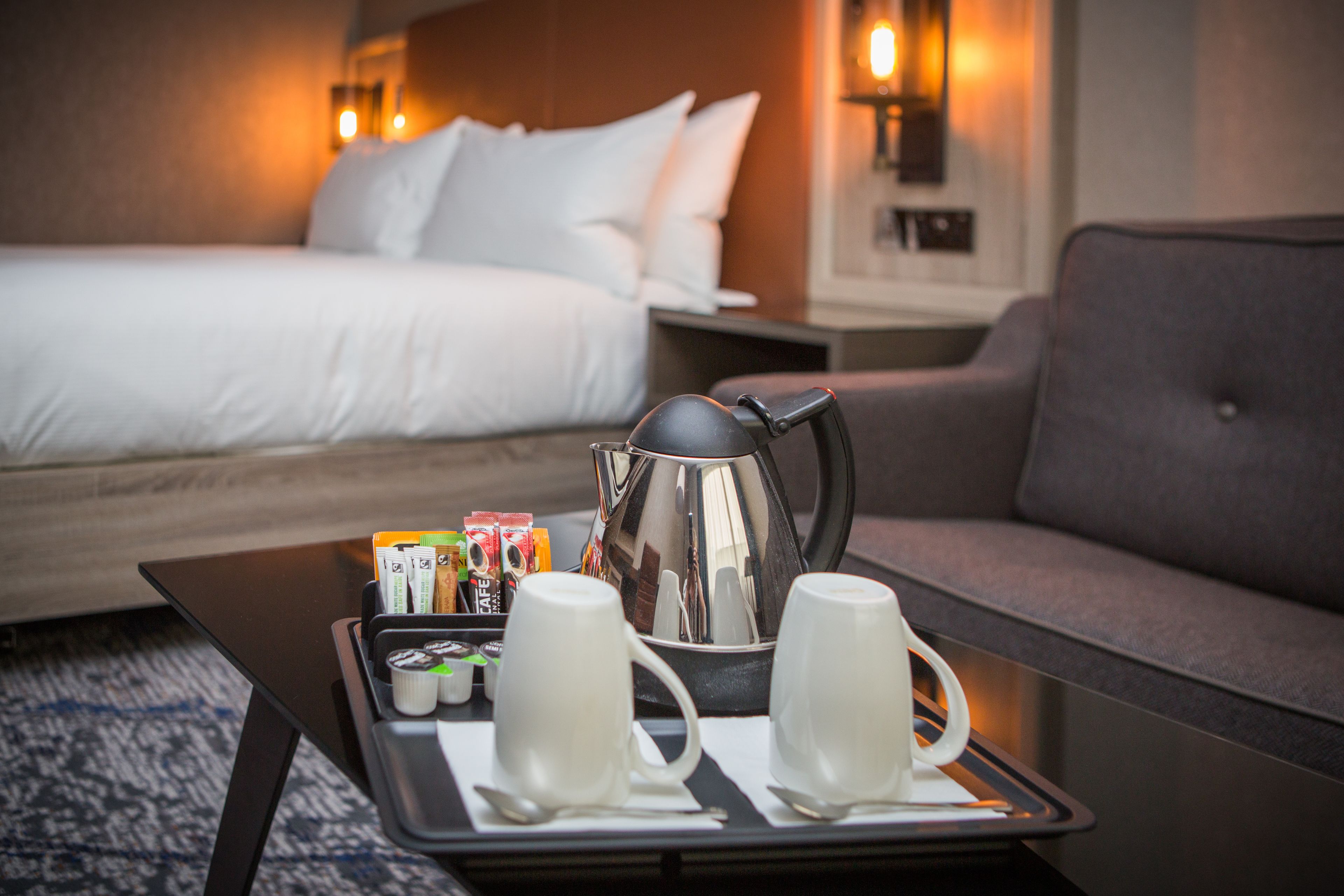 A hotel room with a bed, a sofa, a tray with coffee cups, a coffee pot, and some snacks.