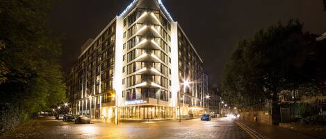 A hotel with a modern design, featuring a prominent corner entrance and a well-lit facade.