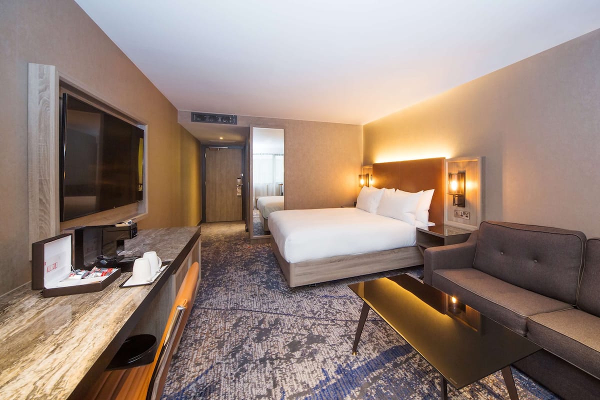 Una habitación de hotel con cama, sofá, televisor, escritorio y piso alfombrado.