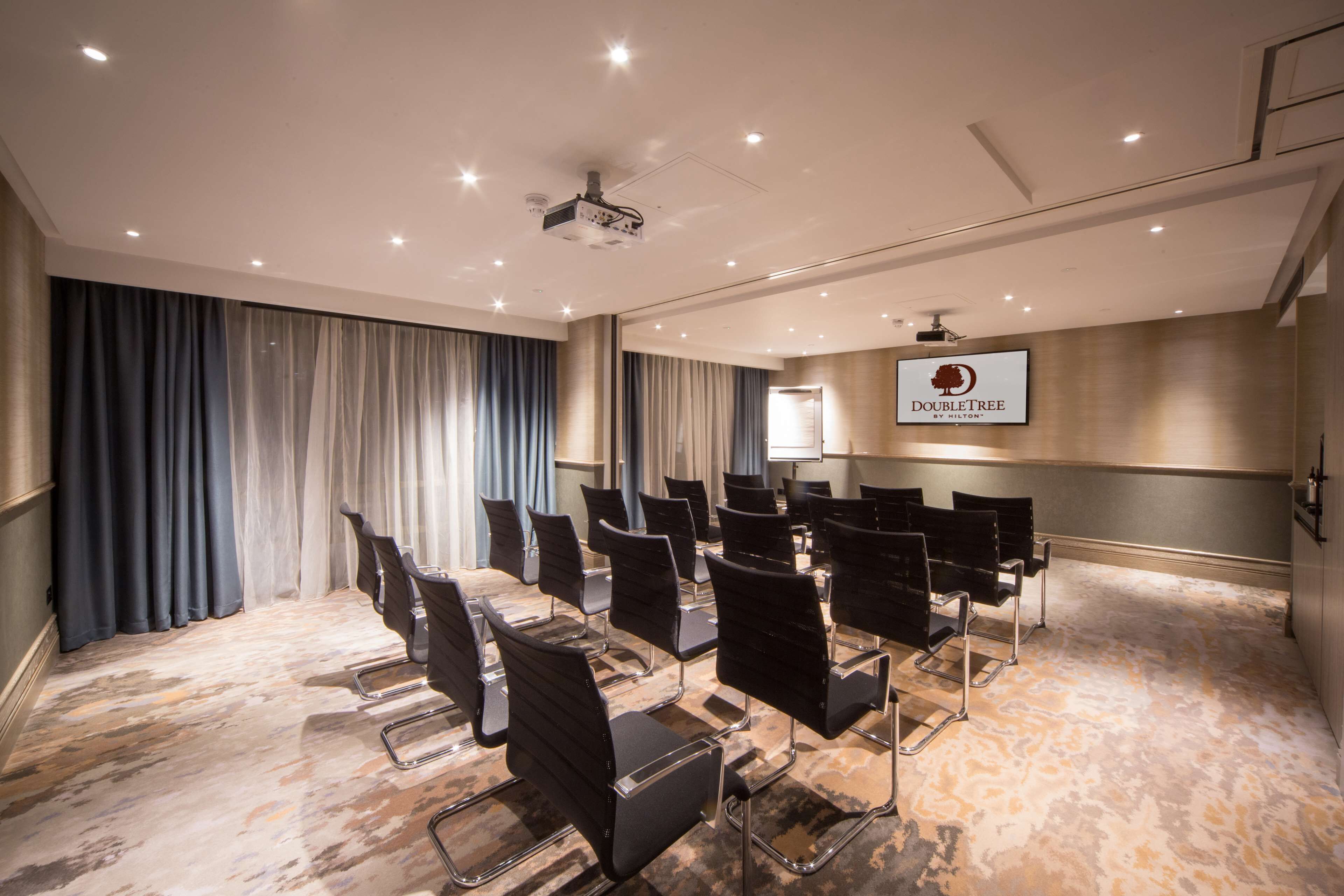 A conference room with rows of black chairs, a projector, and a "DOUBLETREE by Hilton" sign on the wall.