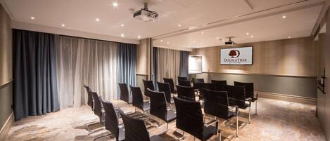 A conference room with rows of black chairs, a projector, and a "DOUBLETREE by Hilton" sign on the wall.