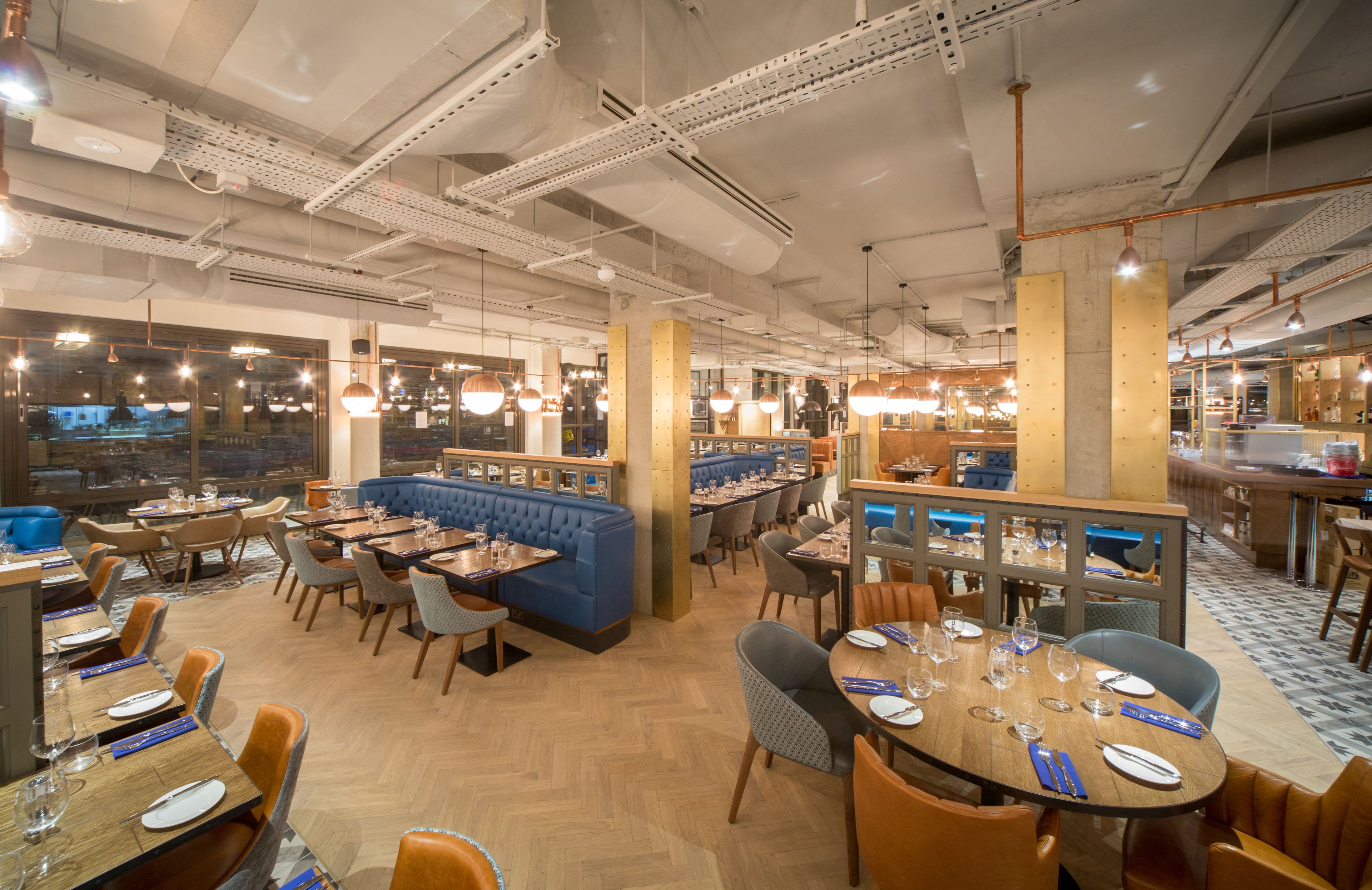 A restaurant with multiple dining areas, including booths and tables, with a modern industrial ceiling and large windows.