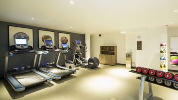 Une salle de sport équipée de tapis de course, de vélos elliptiques et d’une série de haltères.