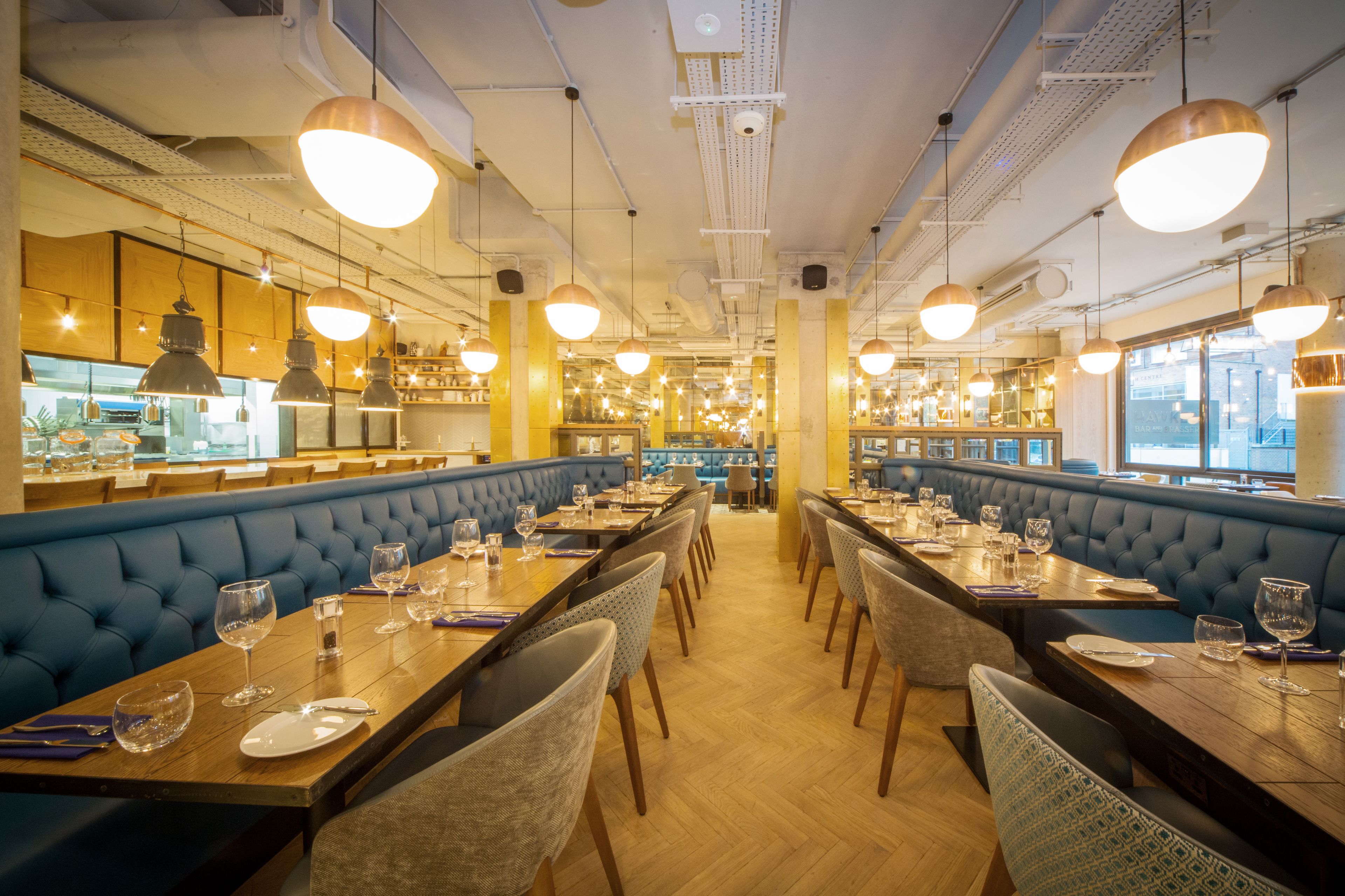 A restaurant with long wooden tables, blue cushioned booths, and pendant lighting.
