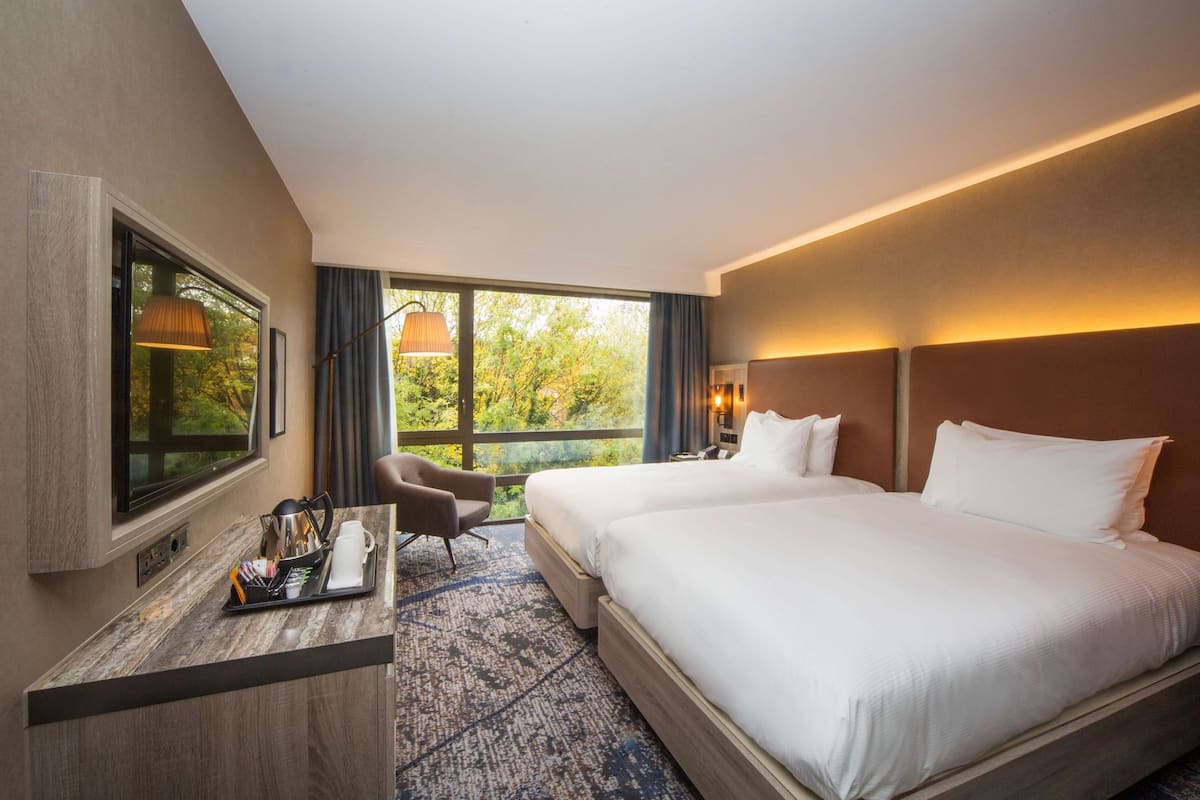 Habitación de hotel con una cama grande, un escritorio con silla, televisor y ventana con vista a árboles.