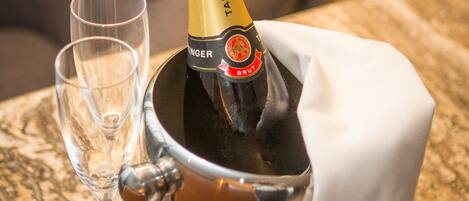 A bottle of champagne in a metal bucket with a white cloth, accompanied by two empty glasses on a marble countertop.