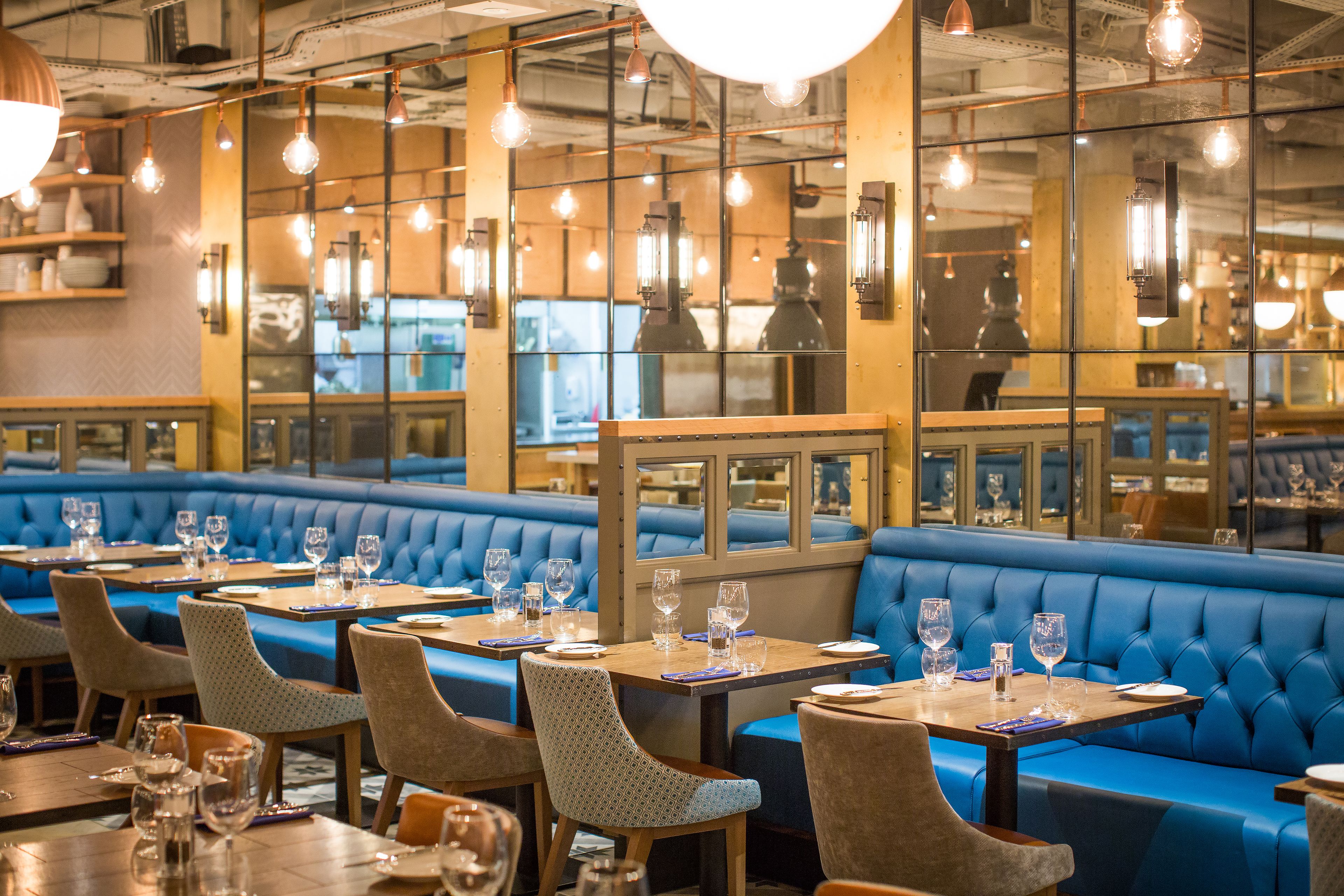 A restaurant with blue cushioned booths, wooden tables, and hanging light fixtures.