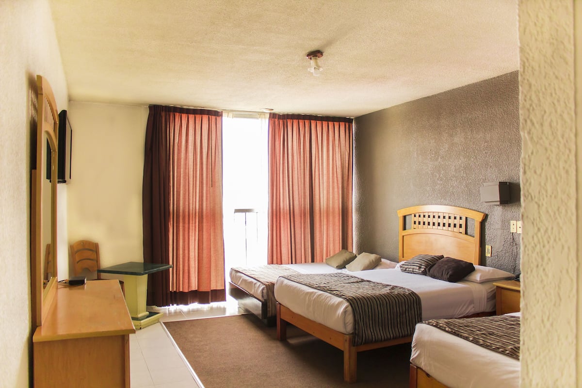 Quarto de hotel com duas camas de solteiro, uma escrivaninha, uma cadeira e uma janela com cortinas.