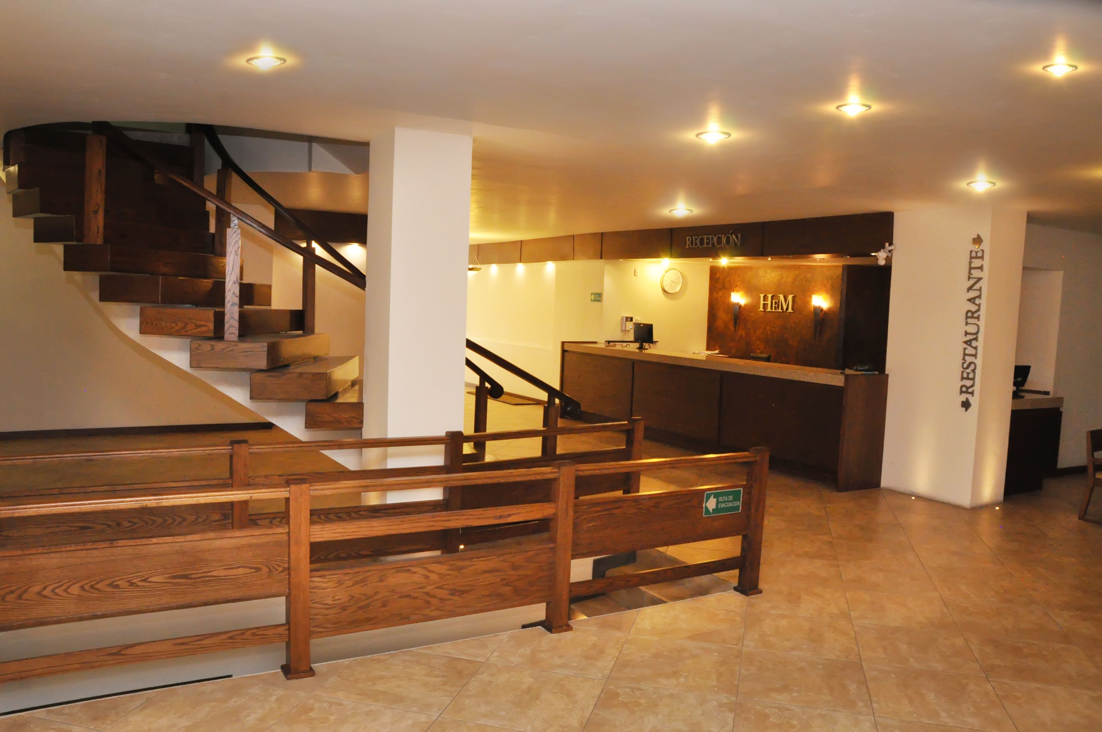 Zona de recepción con una escalera de madera, mostrador de recepción y un letrero para el restaurante.