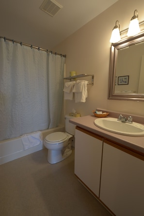 A bathroom with a bathtub, toilet, sink, and a mirror with lights. - The Garrison (Wells)