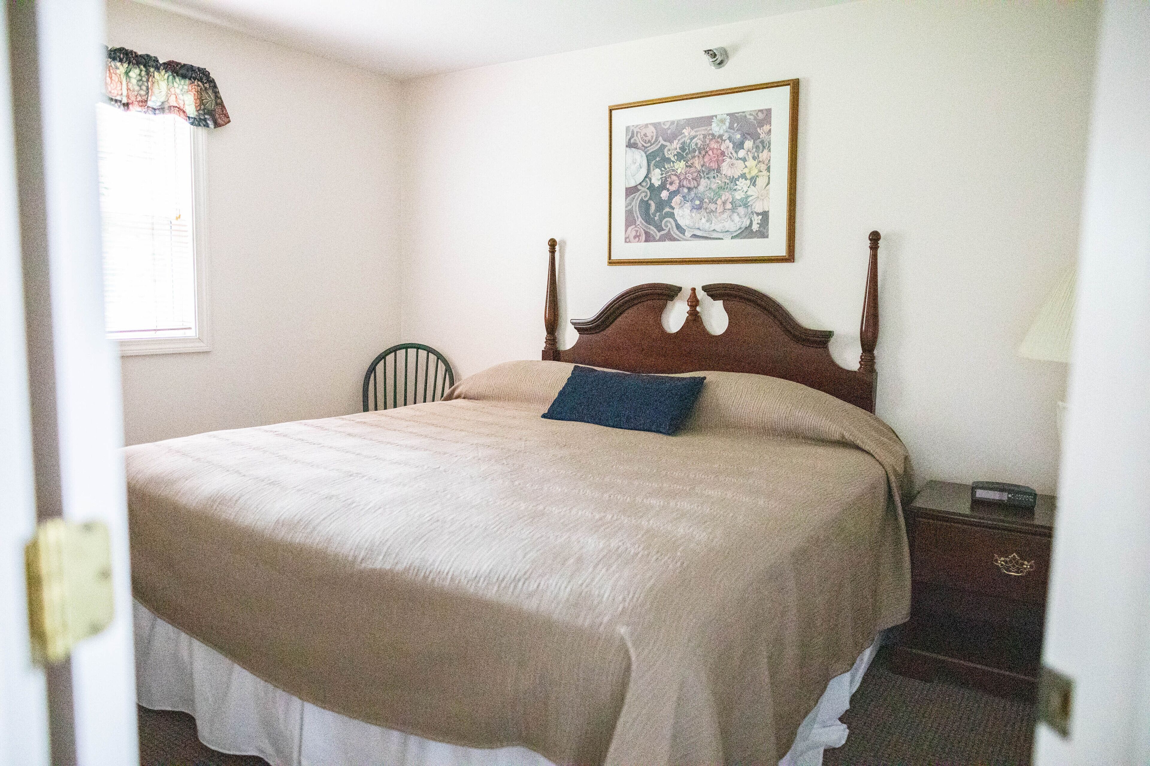 A neatly made bed with a wooden headboard, a bedside table with a lamp, and a framed picture on the wall.