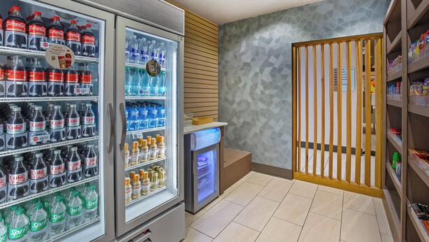 A vending area with Coca-Cola and Sprite bottles, a refrigerator, and a snack shelf. - Holiday Inn Express & Suites Carrollton West by IHG (Carrollton)