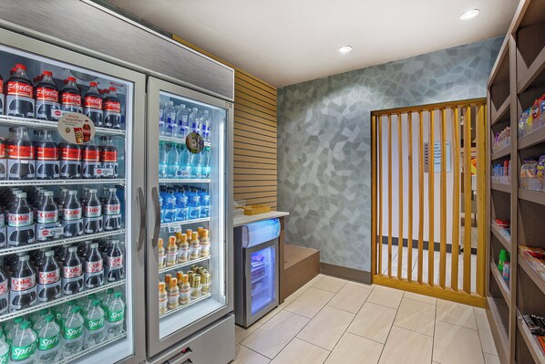 Un área de venta con botellas de Coca-Cola y Sprite, un refrigerador y una estantería con snacks.
